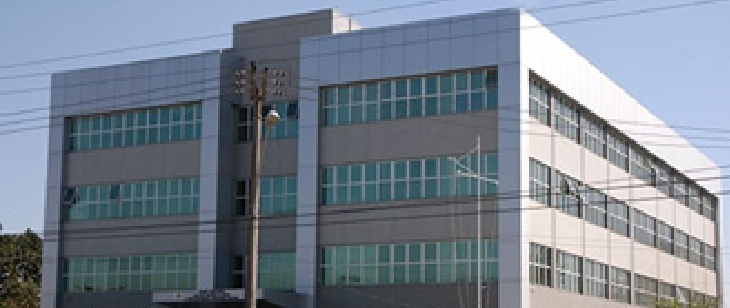 Fachada da 1ª Circunscrição Judiciária Militar, em Brasília. Prédio moderno de quatro andares com fachada cinza e branca, composto por grandes janelas de vidro alinhadas horizontalmente. A construção tem linhas retas e aparência corporativa. Há postes e fiação elétrica visíveis em frente ao edifício.