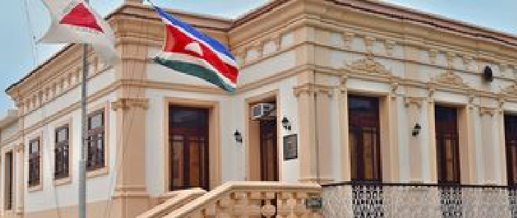 Fachada da 4ª Circunscrição Judiciária Militar, em Minas Gerais. Prédio histórico com escadaria central, janelas altas e colunas ornamentadas. Bandeiras estão posicionadas junto à entrada principal.